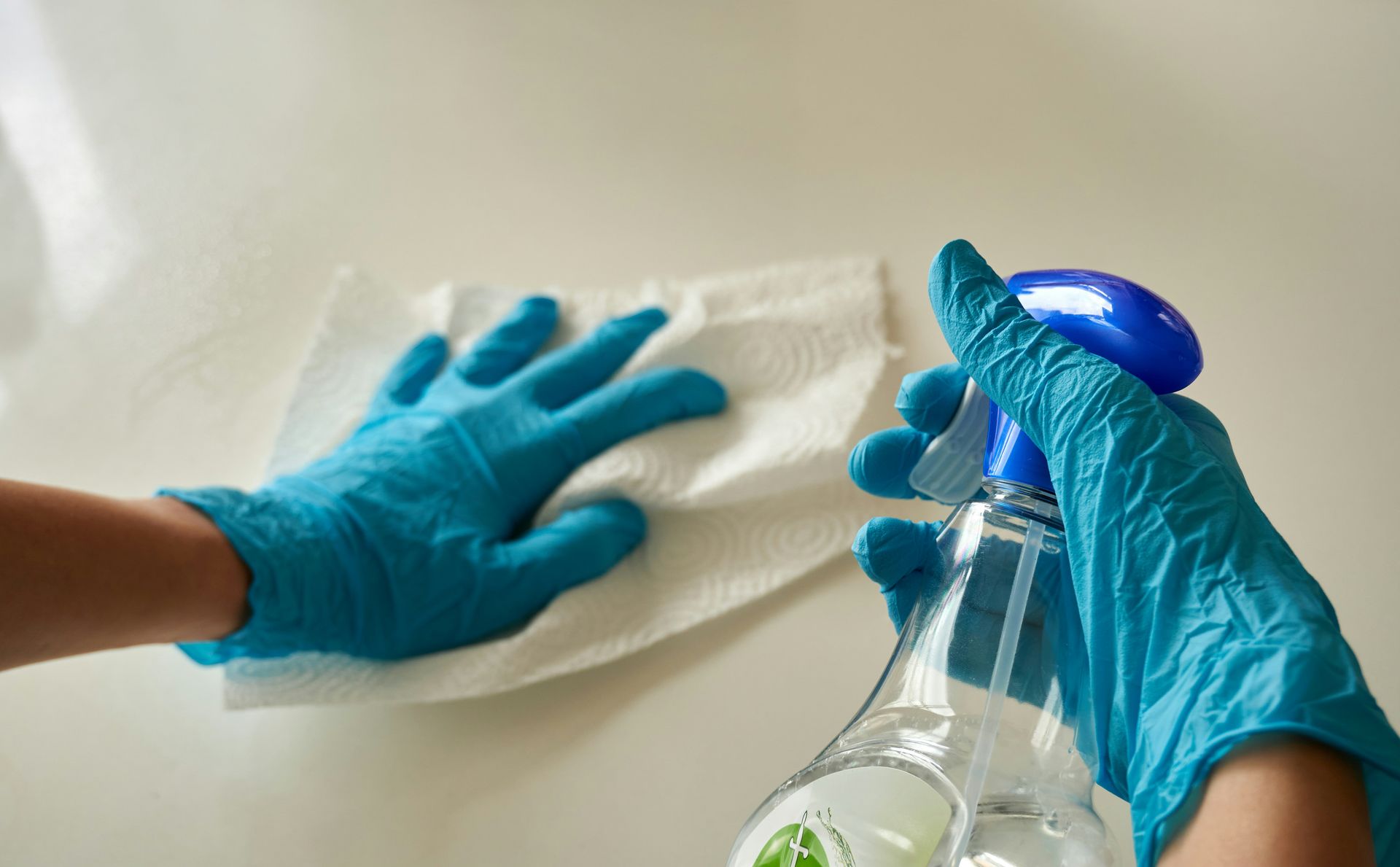 Hands in blue nitrile gloves wiping a white surface with a paper towel