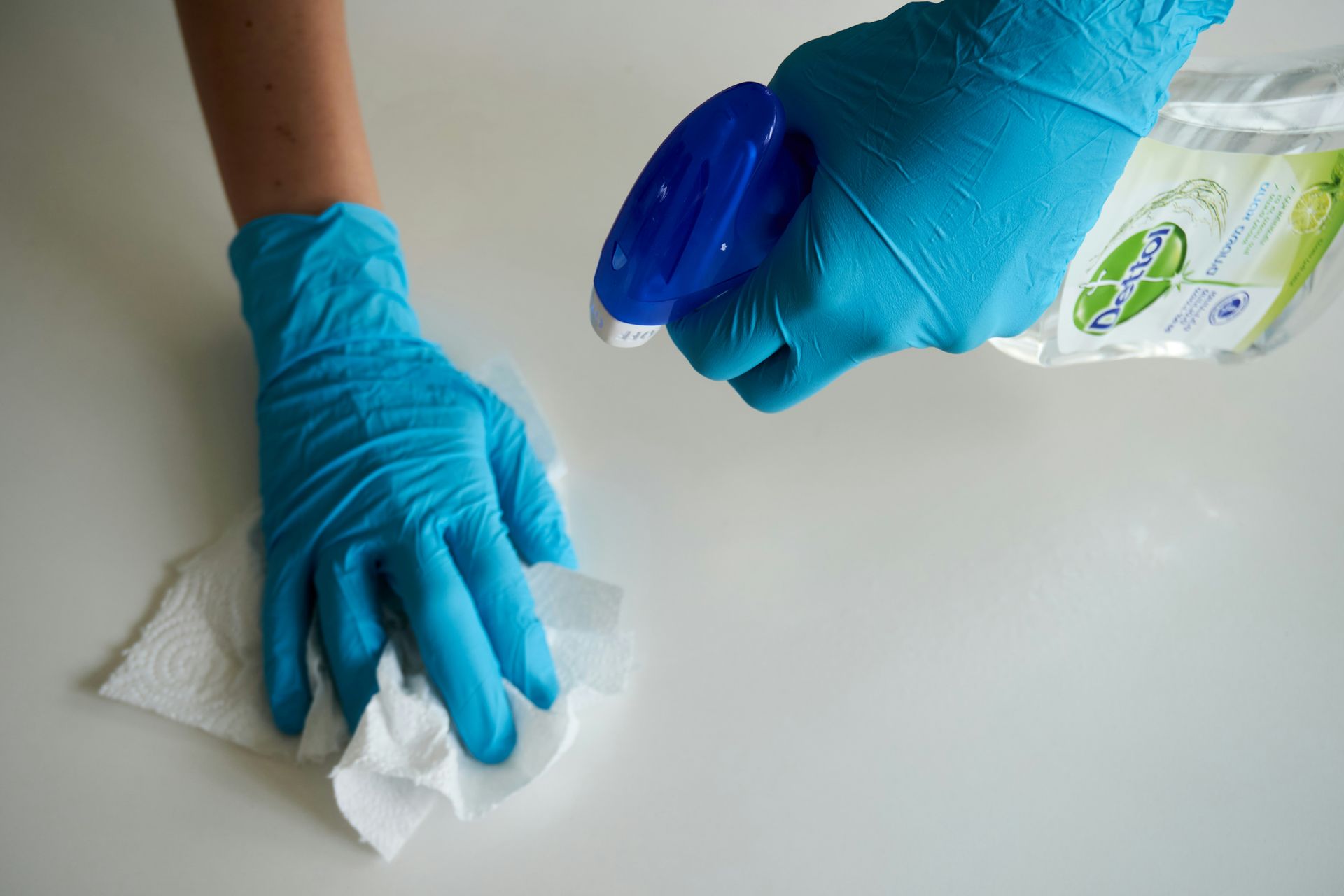 A person in blue gloves wiping a white surface with a paper towel